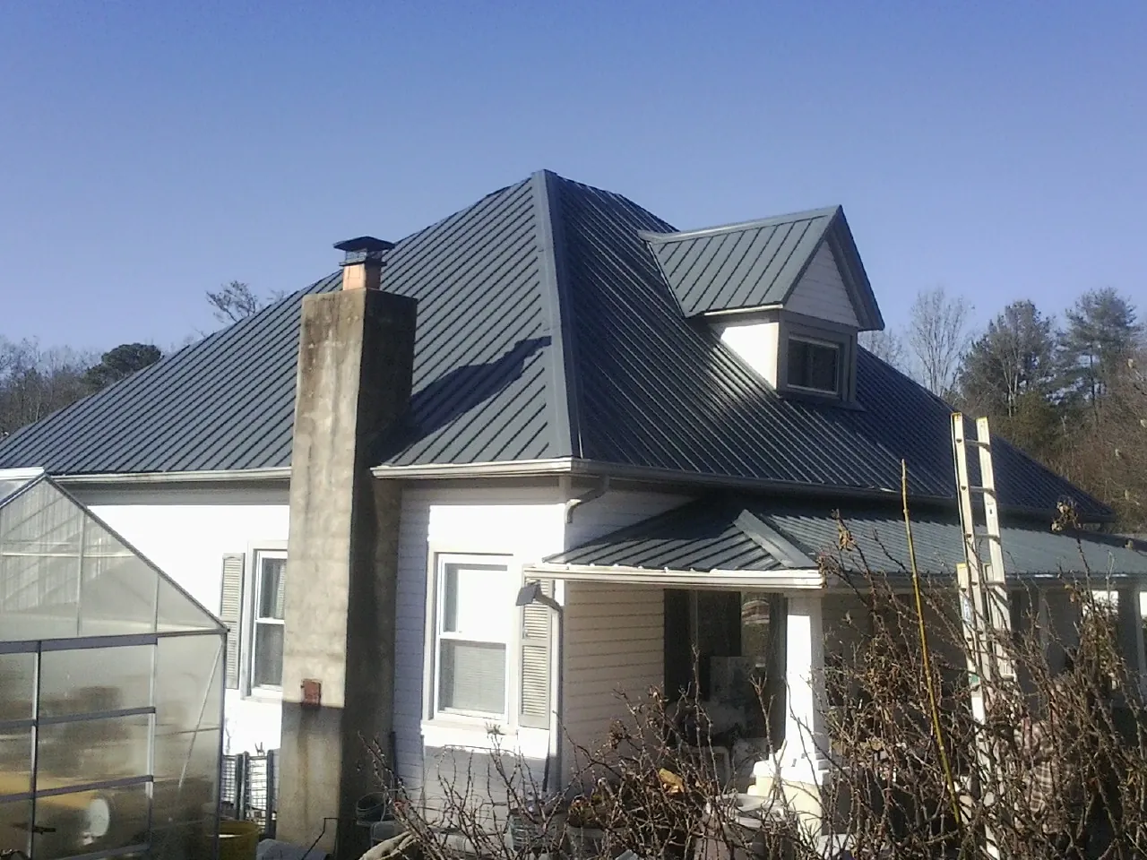 Dark blue standing seam metal roof on a white farmhouse with dormer — Slate & Tile Roof Repair by Roofing Brothers in Cisco