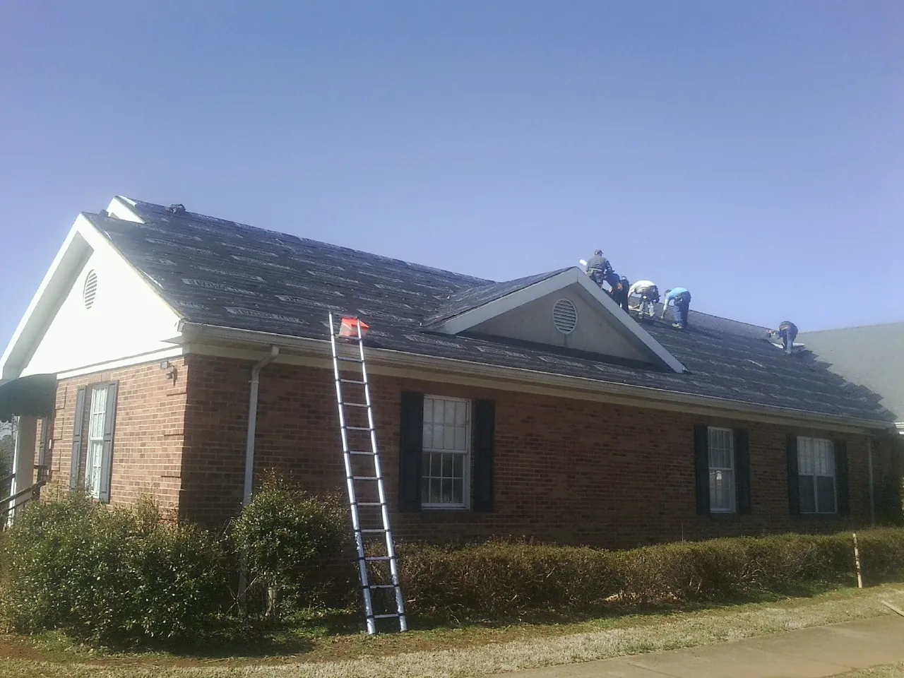 Crew tearing shingles off a brick ranch roof with a ladder set — Emergency Roof Repair work by our crew in Cisco