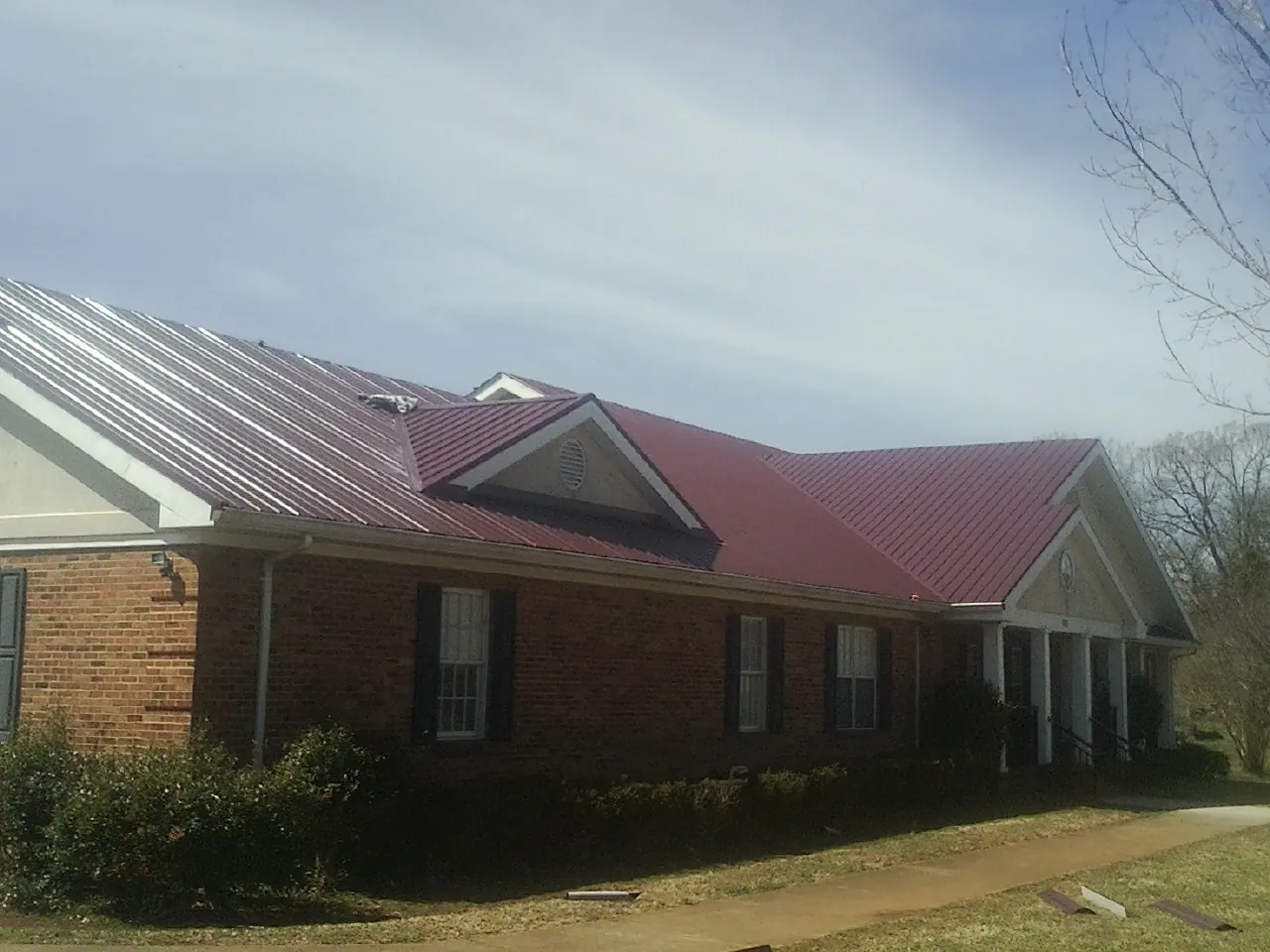 Red metal roof with gabled entries on a long brick building, from a Hail Damage Roof Repair job in Cisco
