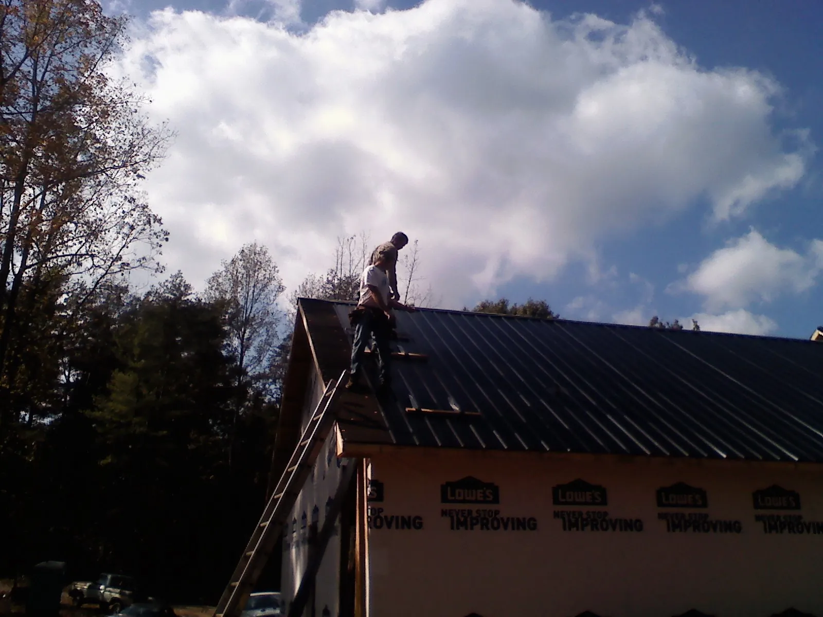 Roofer fastening dark metal panels high against a cloudy sky, from a Roof Inspection job in Cisco