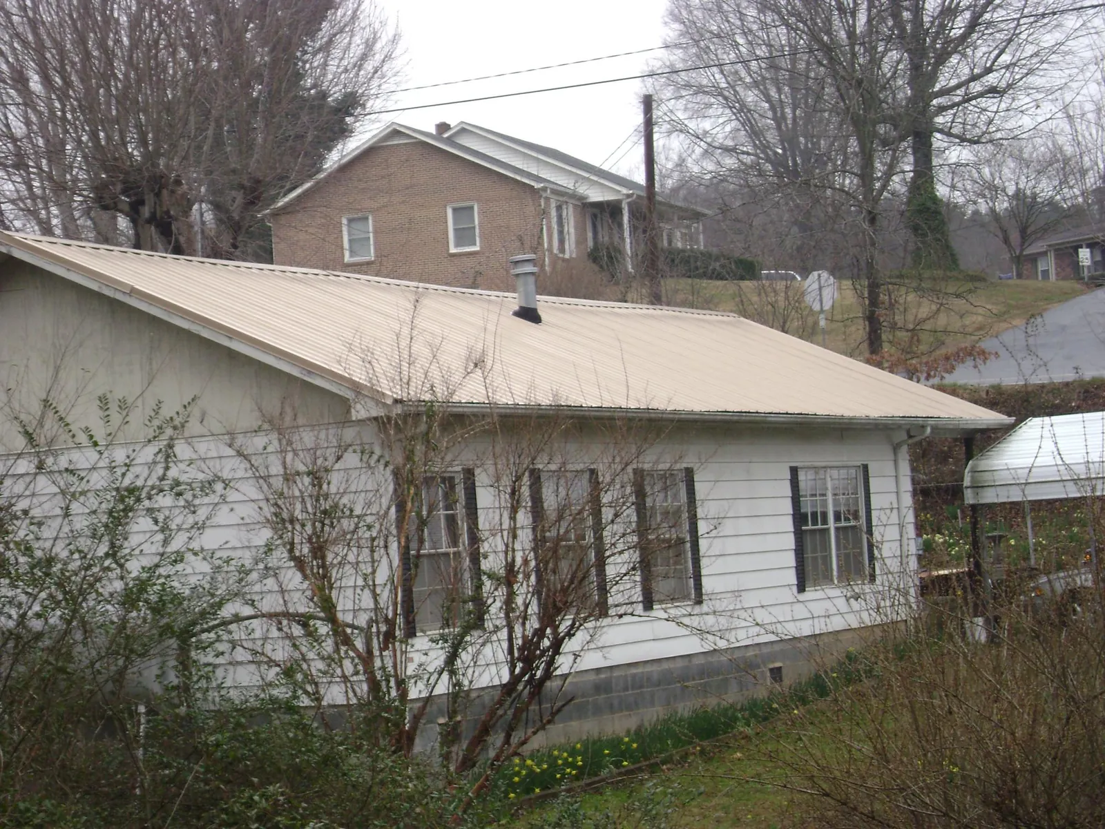 Tan metal roof on a white sided house set into a hillside — Commercial Roofing by Roofing Brothers in Cisco